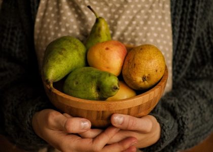 Close-up of hands holding a wooden bowl filled with pears and apples in warm indoor lighting.